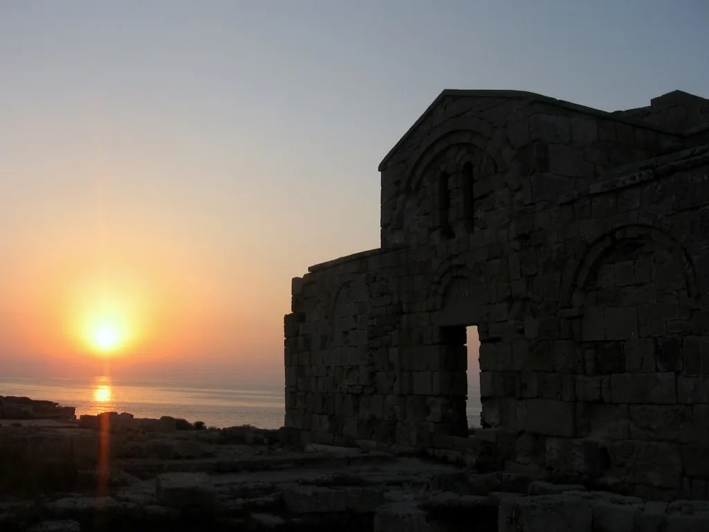 A front view of the historical church at Agios Filon, with the sea and setting sun behind it.