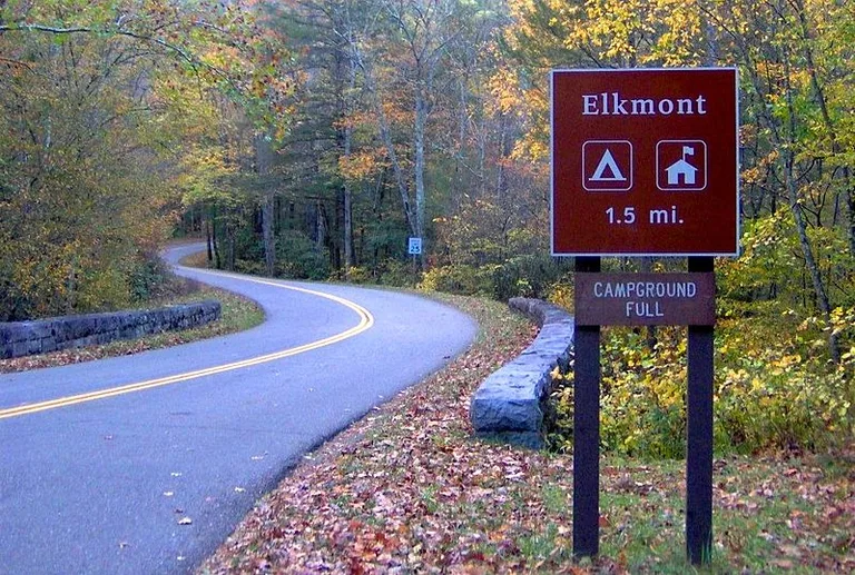 Sign post showing Elkmont Campground ahead. There is a lush autumn forest by the road.